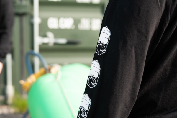 Arm of long sleeve black t-shirt with bearded men adventures logo.
