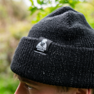 Man wearing black wool beanie hat with bearded men adventure label.